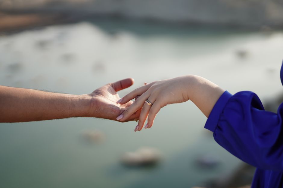 Hands reaching out for connection by a blurred water landscape, symbolizing love and intimacy.