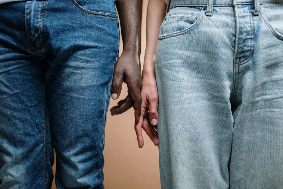 Close-up of an interracial couple holding hands, showcasing unity and diversity in denim jeans.