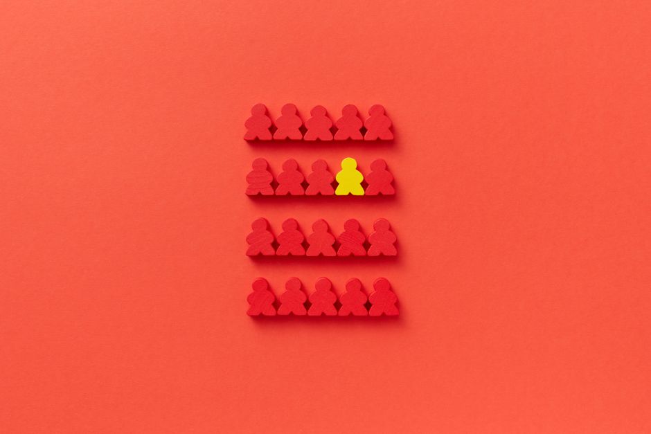 A standout yellow game piece among red pieces on a red background highlighting individuality.