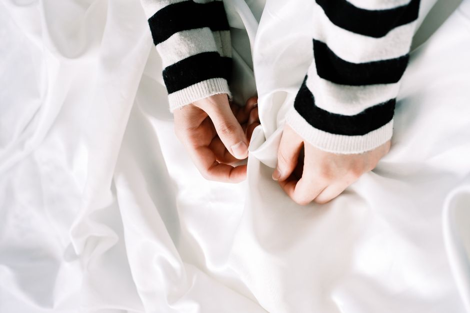 Close-up of hands in striped sleeves grasping white fabric, conveying texture and minimalism.