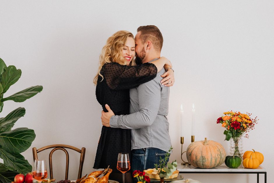 Caucasian couple embracing during a cozy Thanksgiving dinner with autumn decorations.