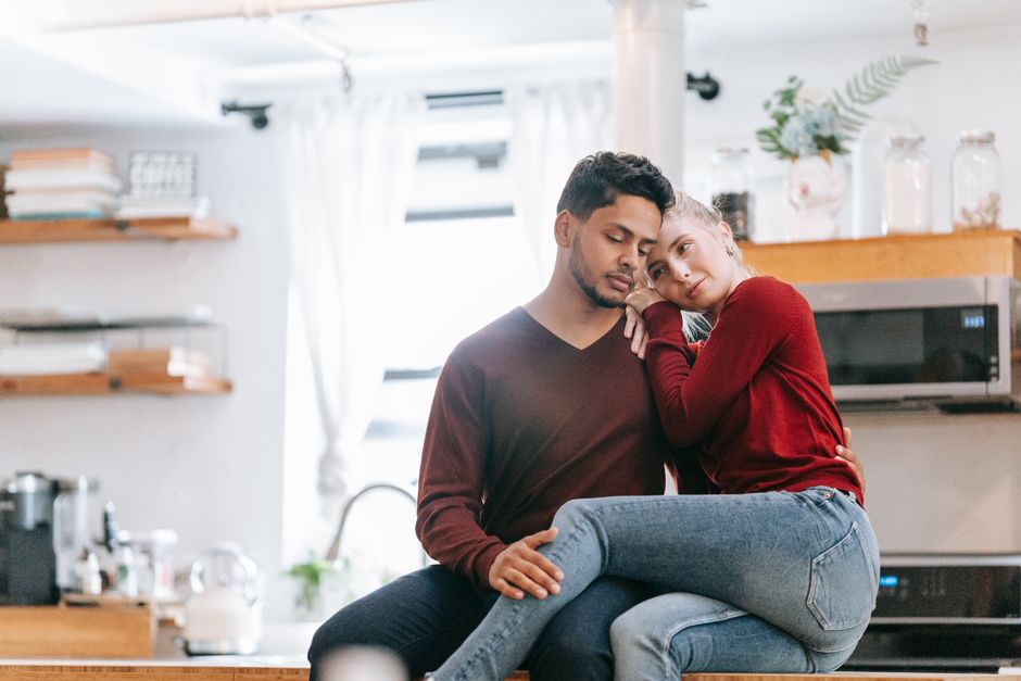 A couple lovingly embrace in a bright, modern kitchen setting.
