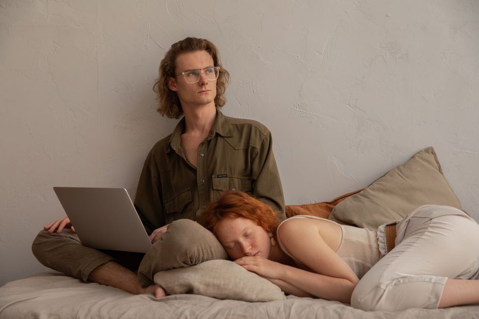 Man with laptop and woman relaxing on bed, perfect for remote work and lifestyle themes.