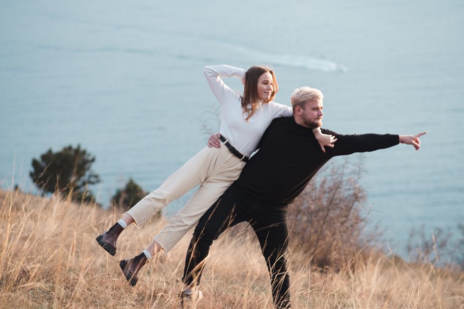 Joyful couple enjoying a playful moment on a grassy hillside by the sea.