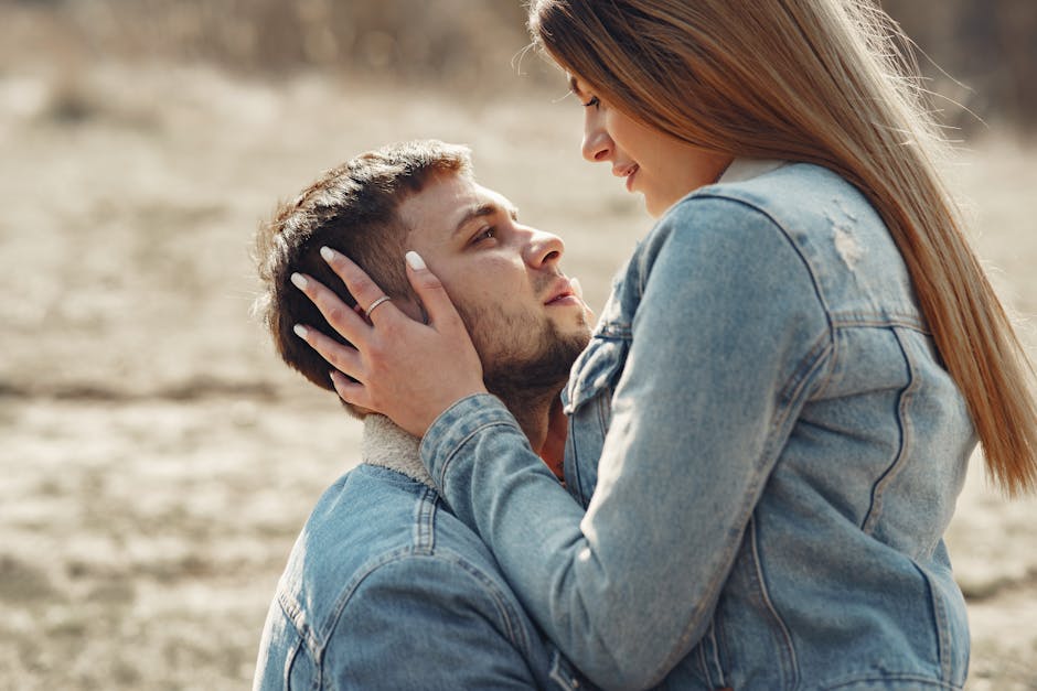 Side view of loving young couple in denim jackets hugging and looking at each other while spending time together on grassy meadow in countryside